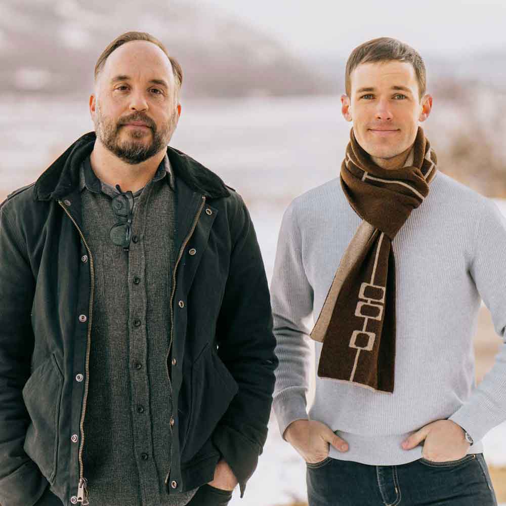 Two of the agents on the Hanson Team, Joshua Brown and Carson Carter, are pictured from the waist-up in front of the Hudson River during the winter.